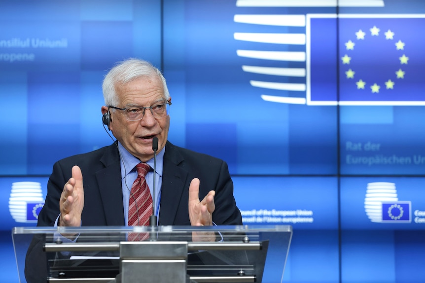 Un uomo dai capelli grigi mostra un pulpito davanti al cartello dell'Unione europea