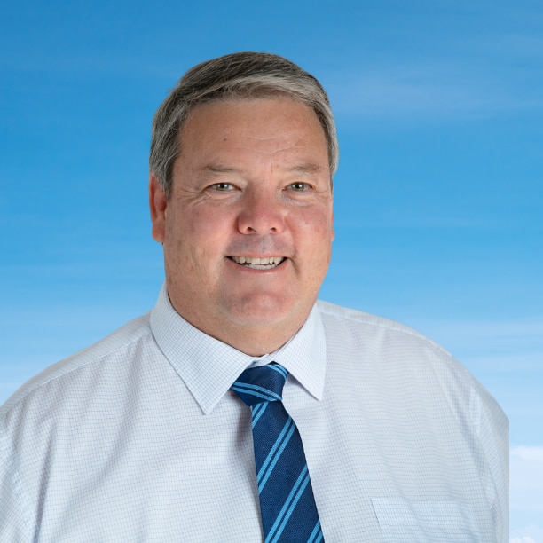 A man in a white dress shirt and blue tie smiles.