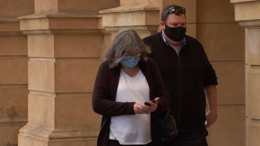 A woman and a man wearing face masks outside a stone building