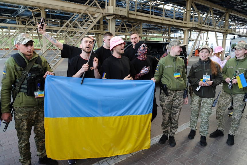 Kalush Orchestra holding up a Ukrainian flag with a group of solders. 
