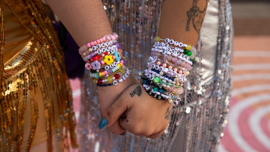 Two women in sequin dresses with a dozen beaded bracelets each hold hands