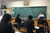 A teacher wearing a pink traditional dress from North Korea stands in front of a blackboard filled with algebra.