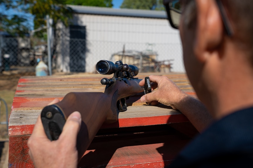 A man inspects the empty magazine of a rifle on top of a stack of pallets.