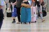 An unidentified person rolls a suitcase and carries a coles bag through the Brisbane Airport.