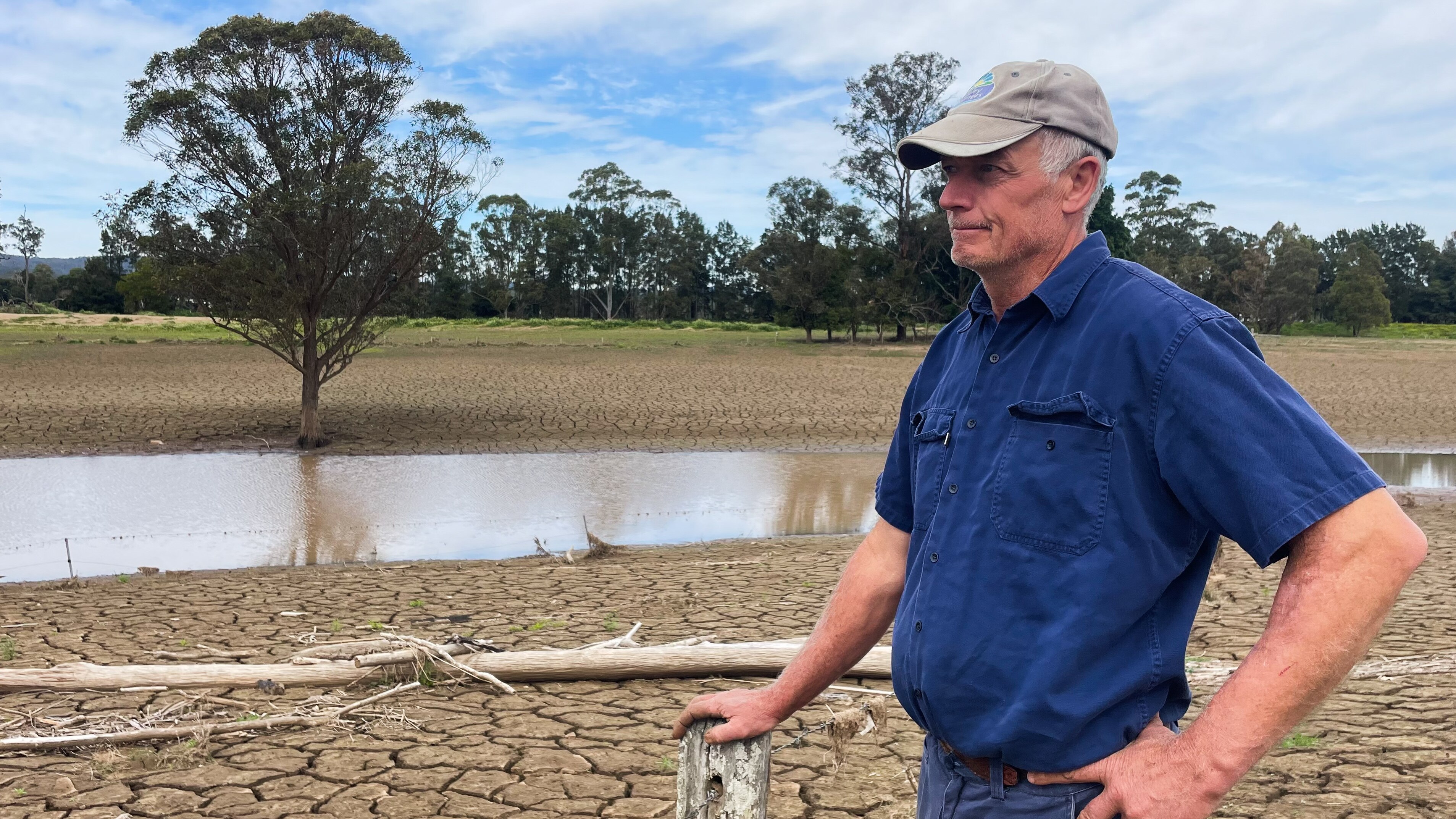 Man leaning on old fence post, with cracked ground around him. 