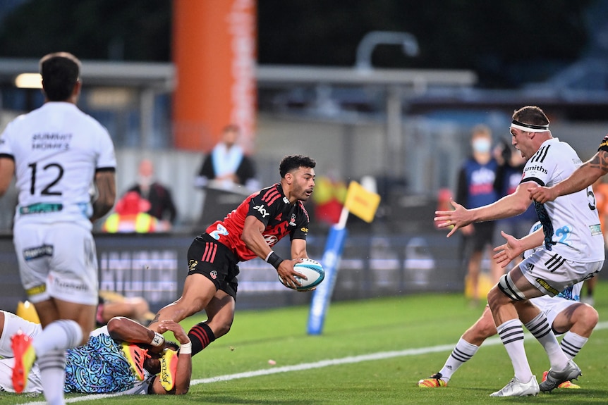 A Super Rugby player braces himself holding the ball while he is held in an ankle tackle while more defenders close in.