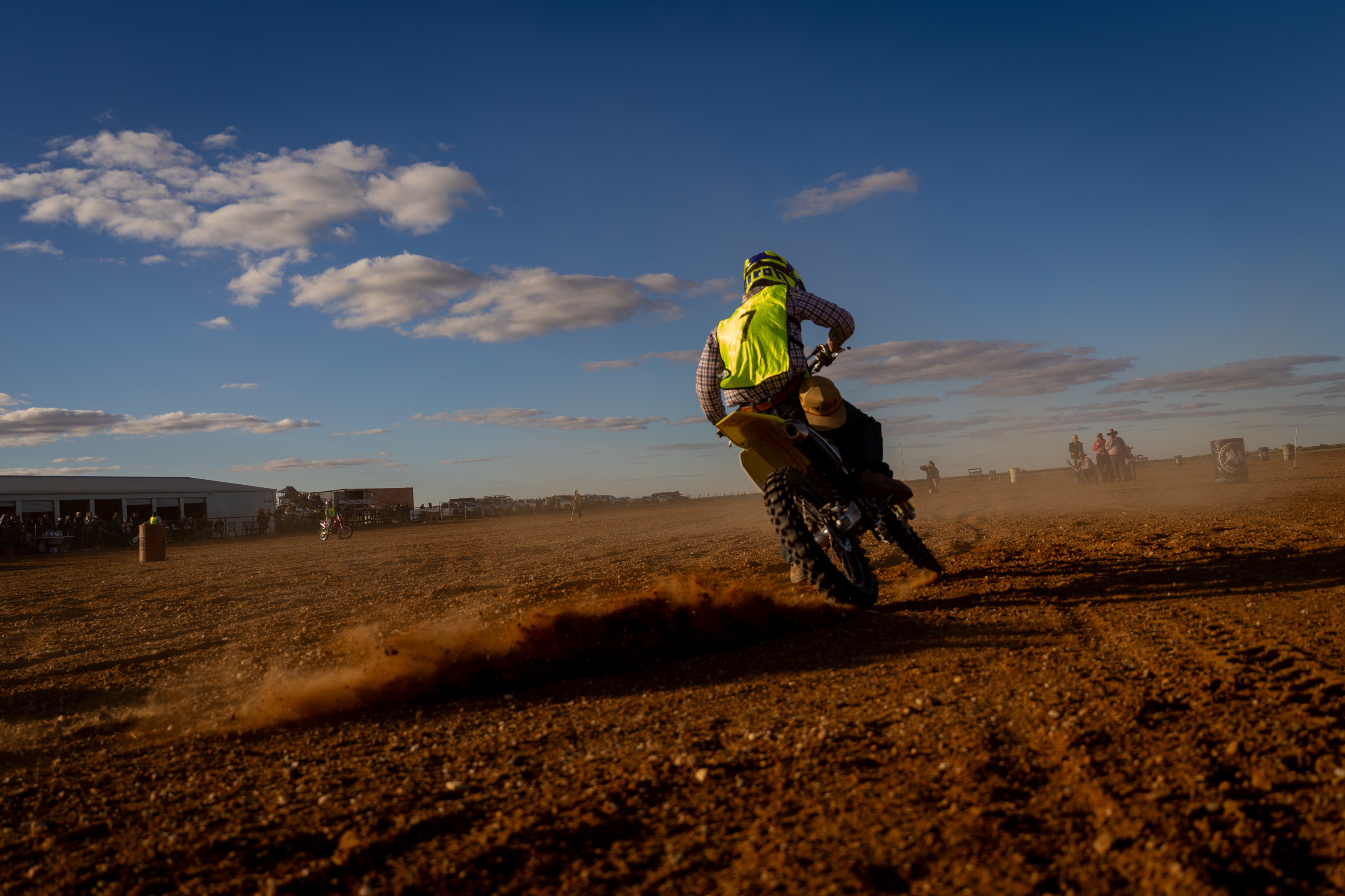 A person riding a motorbike away from the camera, with dust coming up behind the wheel