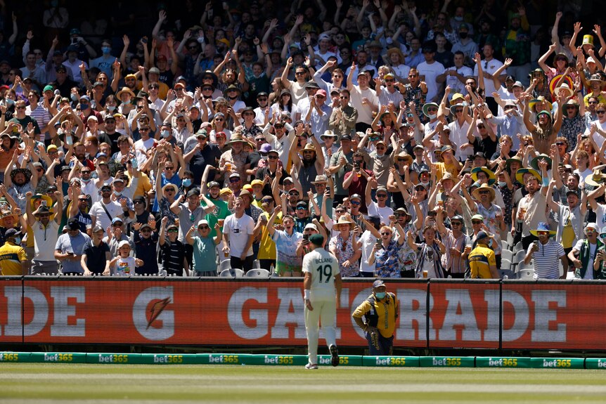 A massive crowd rise to their feet to applaud Scott Boland, who is standing near the boundary