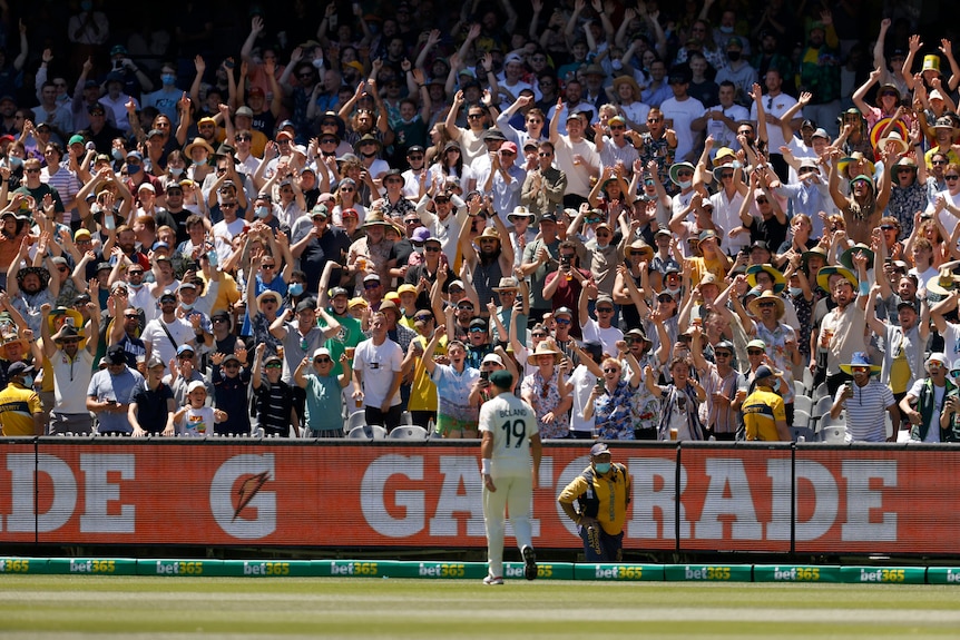 A massive crowd rise to their feet to applaud Scott Boland, who is standing near the boundary