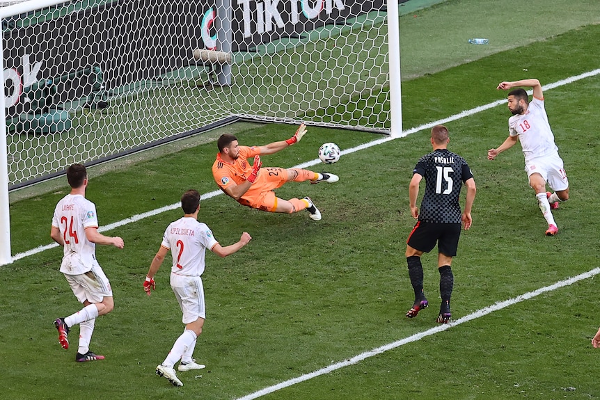 Unai Simon dives to his right and saves a ball that is going to his left.