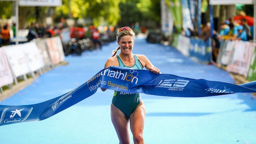 Kate Næss is wearing a green one piece swimming costume, and smiles as she breaks through the finish line. 