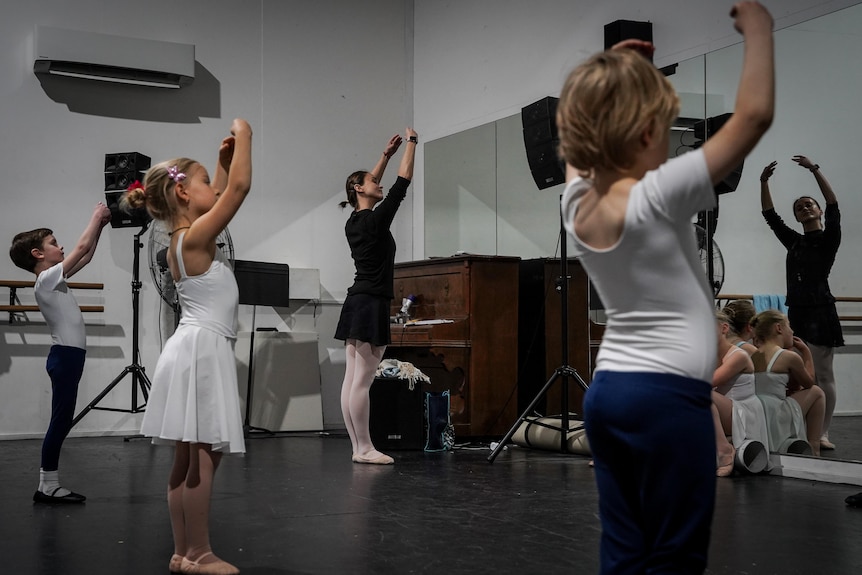 Students hold their hands above their heads in a ballet class.