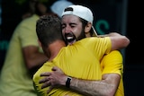 An Australian tennis player wearing his cap backwards, shouts with joy as he hugs his coach after a big win.