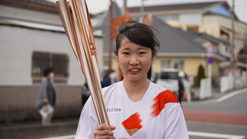 Girl with dark hair wearing white shirt holds gold olympic flame