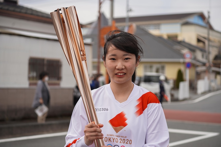 Girl with dark hair wearing white shirt holds gold olympic flame