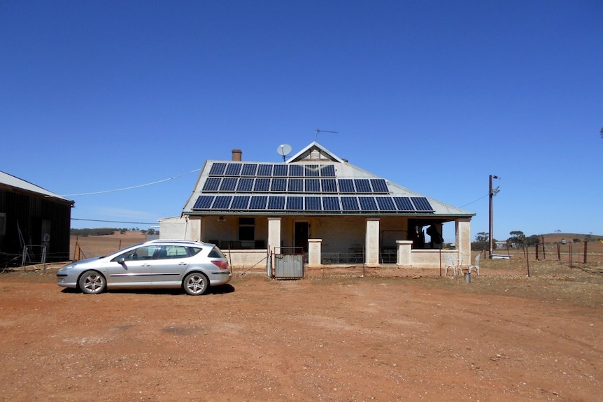 A house on a large patch of red dirt has 30 solar panels stuck to its roof.