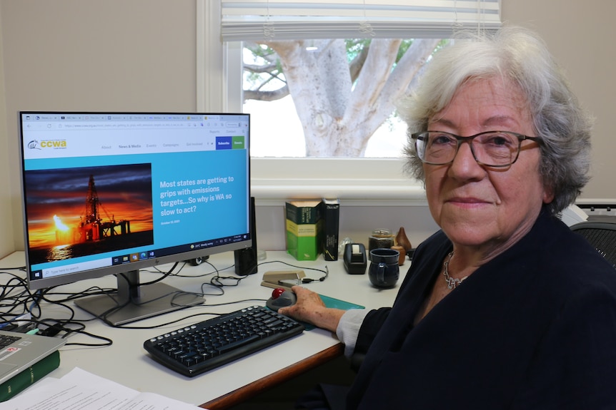 Carmen Lawrence sentada en un escritorio con computadora que muestra la imagen de la plataforma de gas