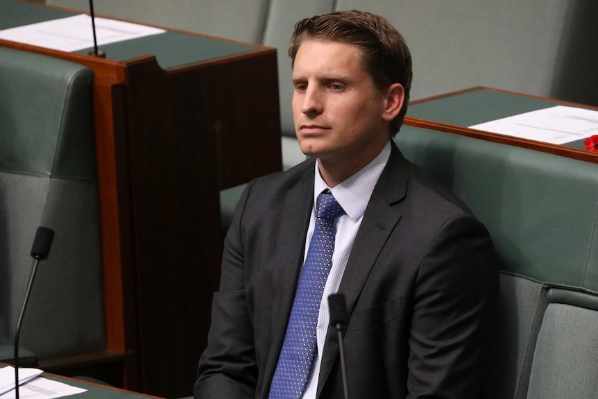 Liberal MP Andrew Hastie sits in the House of Representatives. He has a blank expression, and is wearing a blue shirt and tie