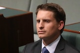Liberal MP Andrew Hastie sits in the House of Representatives. He has a blank expression, and is wearing a blue shirt and tie