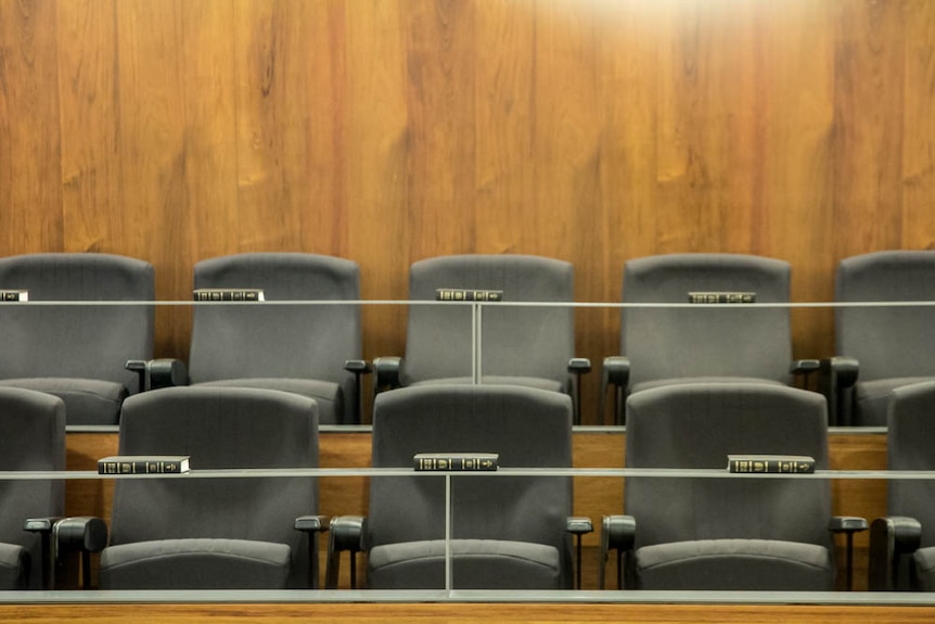 Two rows of seats. On ledges in front of each row, bibles are spaced evenly along. Wood panelled wall in background.