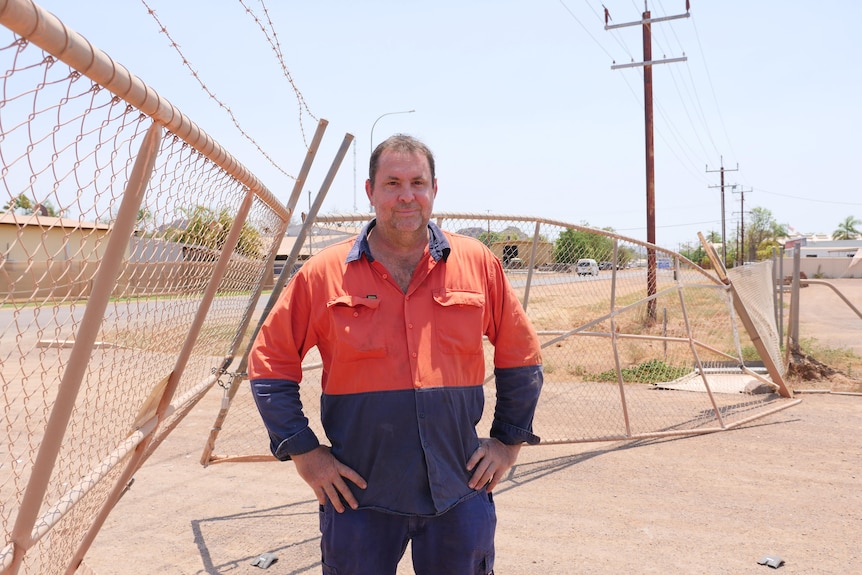 man in high vis stands in front of broken gate