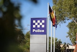 A police sign surrounded by trees, with a row of flags behind it.