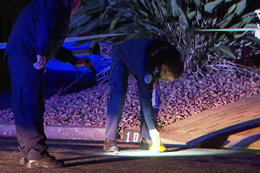 Two police officers place a marker on the ground at the crime scene