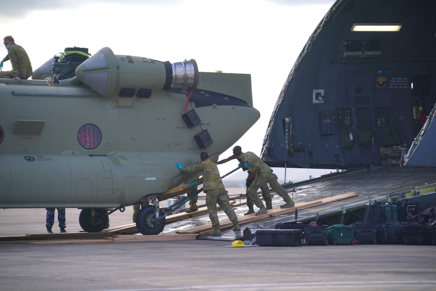 Soldiers manually push the back of a Chinook as it's unloaded from an American cargo plane.