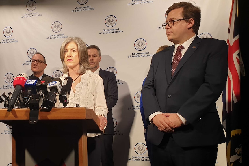 A woman speaks at a dais at a press conference next to a man in a suit