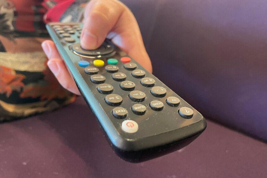A person holds a TV remote while sitting on a couch. 