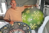 A man in glasses smiles while holding two large christmas decorations 