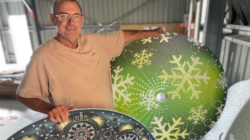 A man in glasses smiles while holding two large christmas decorations 