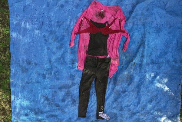 Dirty black clothes and a pink dressing gown are laid out on a blue tarpolin on the ground