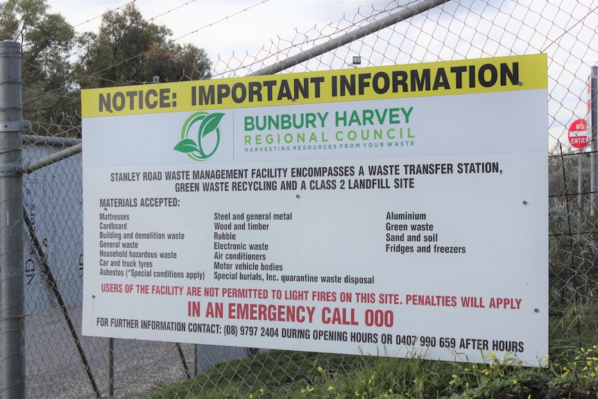 A sign on the a fence at the front entrance to a dump.