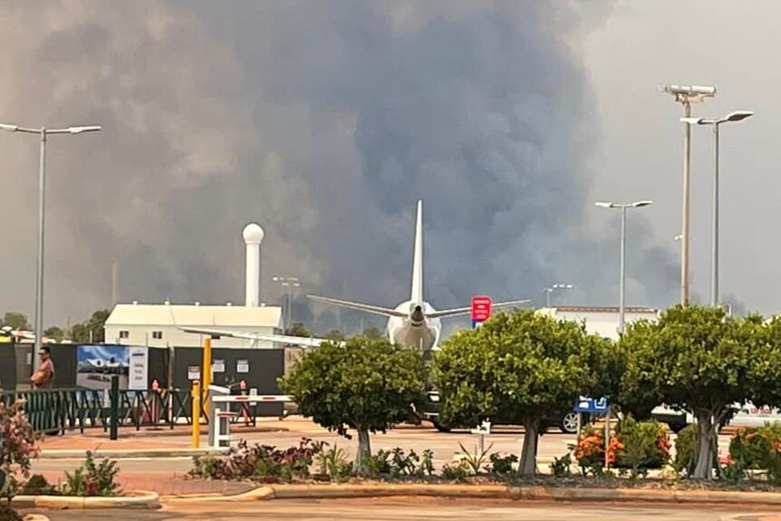 An airport with large smoke billowing in the background.