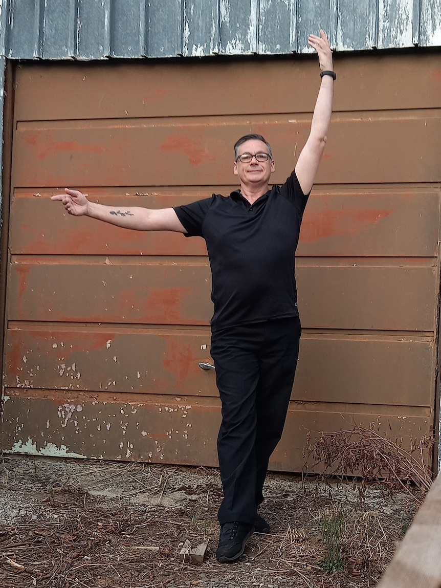 Robbie Bayliss demonstrates a figure skating position standing in front of his garage door.