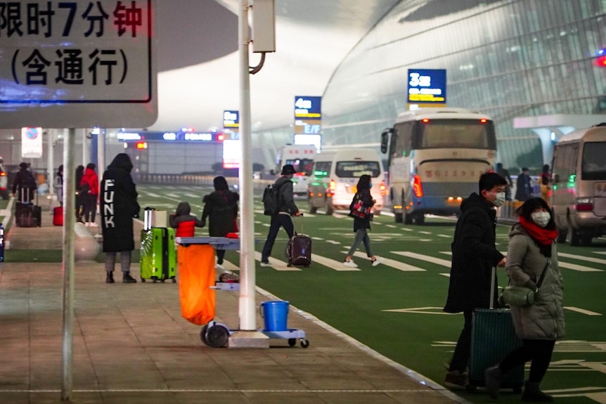 People with masks and luggage at Wuhan airport.