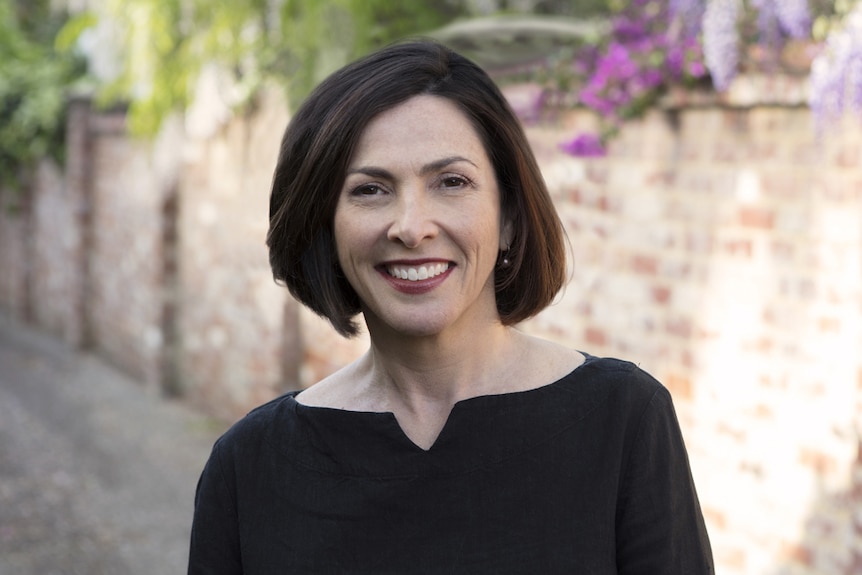 Perth Festival director Wendy Martin, smiling, wearing a black top, outdoors, with a brick wall behind her.