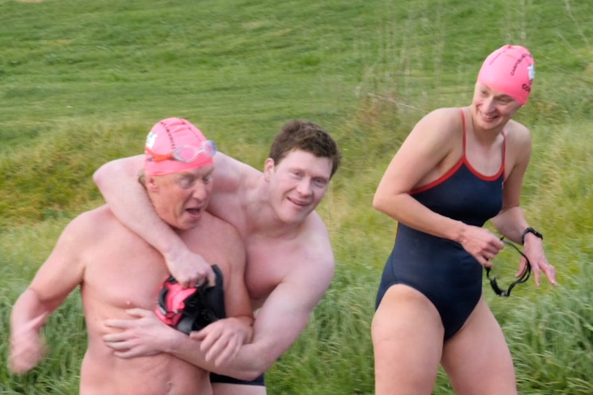 Three swimmers pink skinned with cold smile and hug at the finish of a long swim.