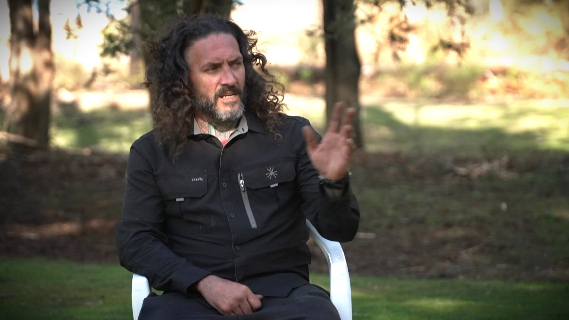 Roy Thomas gestures while sitting in a bushland setting.