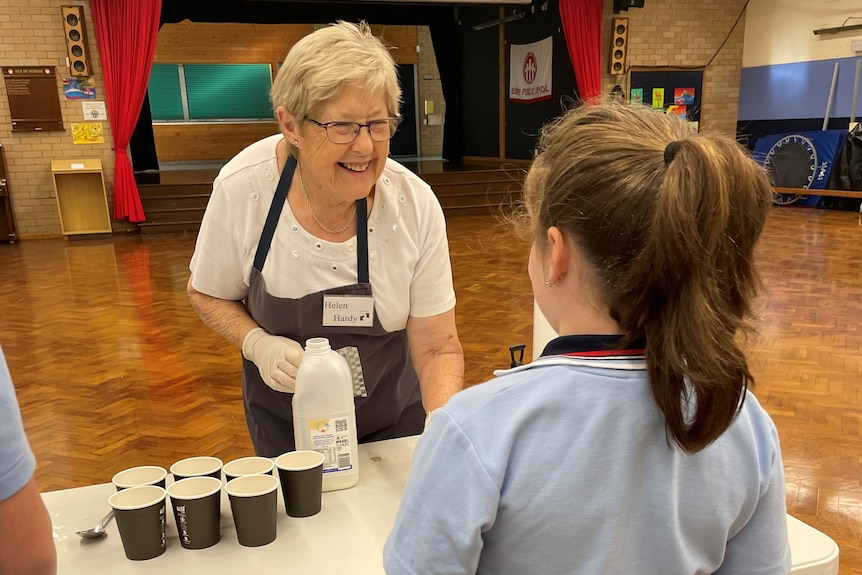 an older woman pours a glass on milk for a primary school student