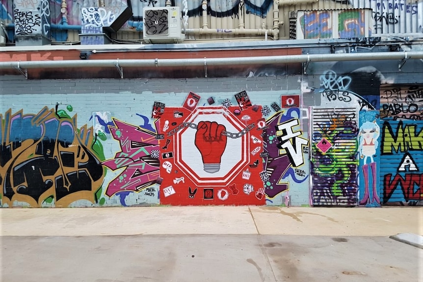 A colourful wall of graffiti and art, with a painting of a large red fist breaking a chain in the centre.