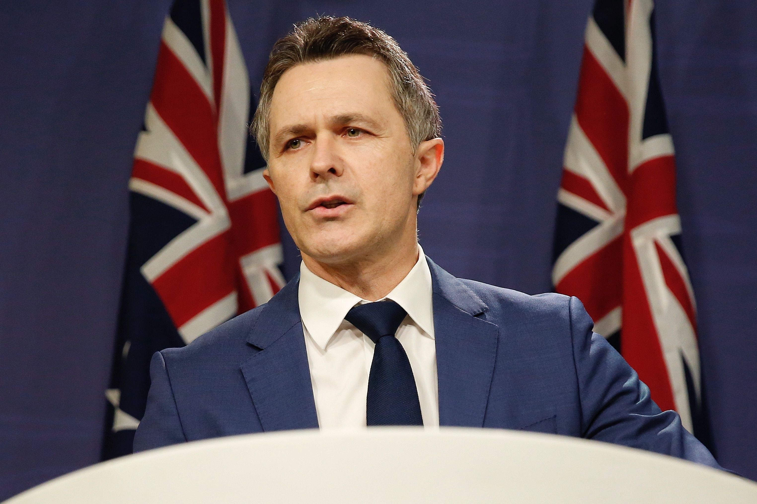Jason Clare speaks at a lecturn in front of Australian flags