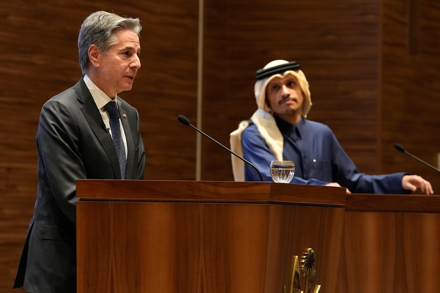 Anthony Blinken stands at a wooden podium with Mohammed Bin Abdulrahman behind him