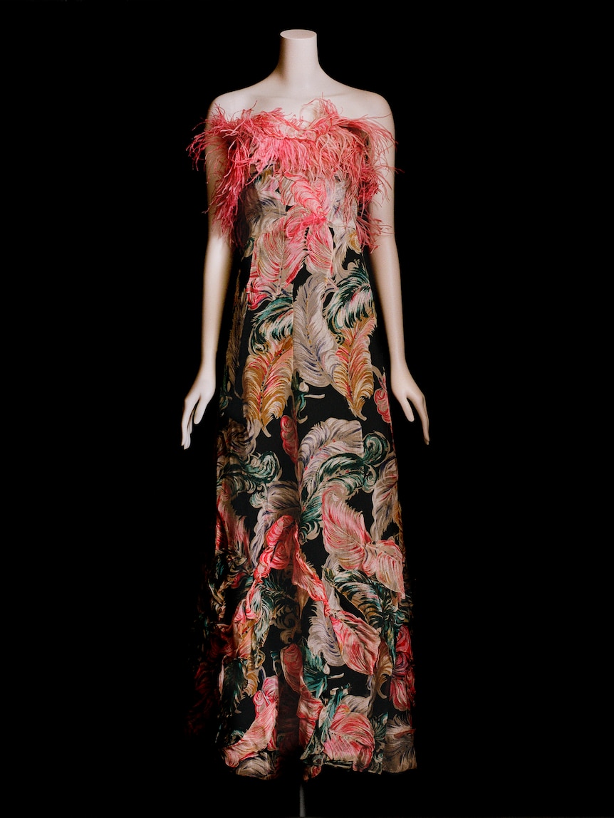 A mannequin in an 1930s evening dress, pink ostrich feathers line the bust and the rest of the dress is printed with feathers