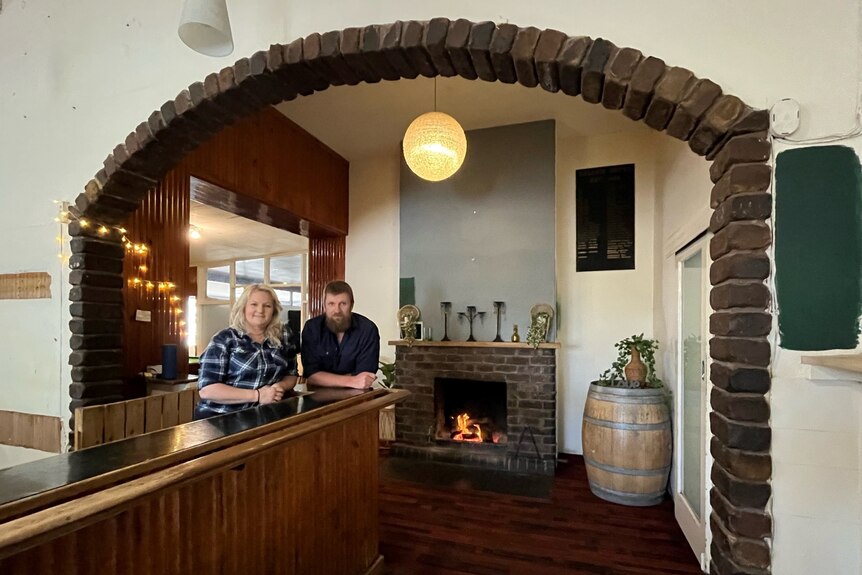 A woman and a man standing at a bar under an arch with a fireplace