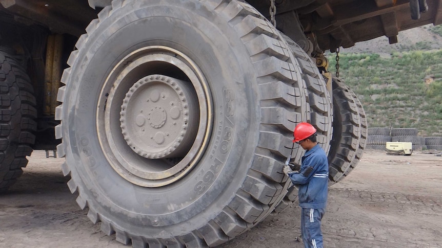 Dump truck with man in hard hat standing in front of rear tyre that is three times his height