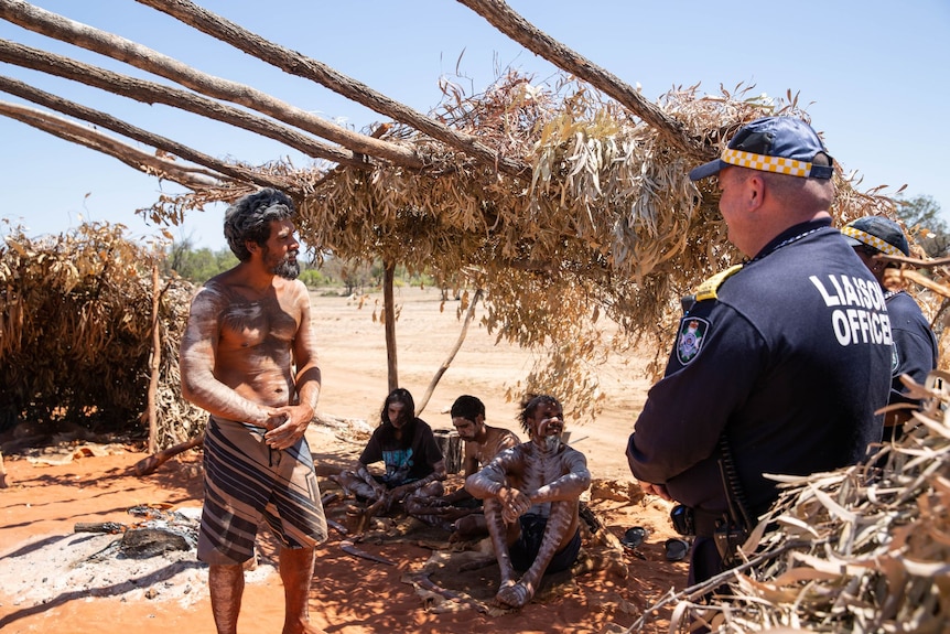 people in traditional indigenous body pain speak with a police officer in a grass hut