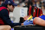 Angus Brayshaw is lying on a stretcher with a neck brace on and his eyes closed