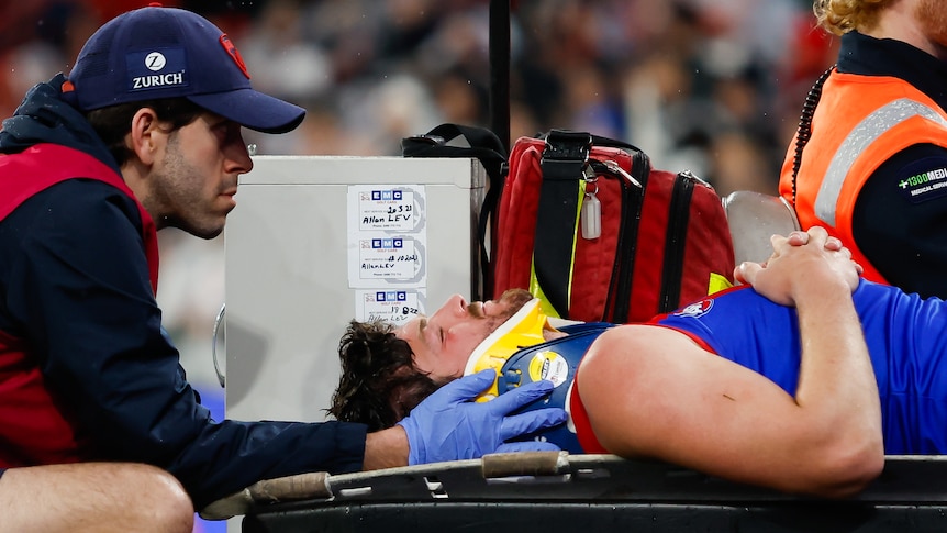 Angus Brayshaw is lying on a stretcher with a neck brace on and his eyes closed